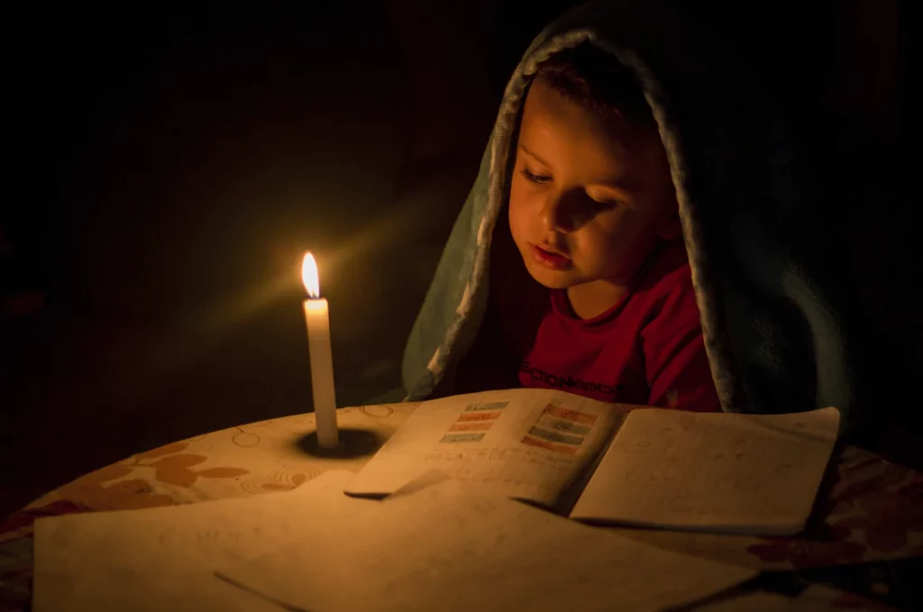 Lapsi lukee kynttilänvalossa energia pulan takia